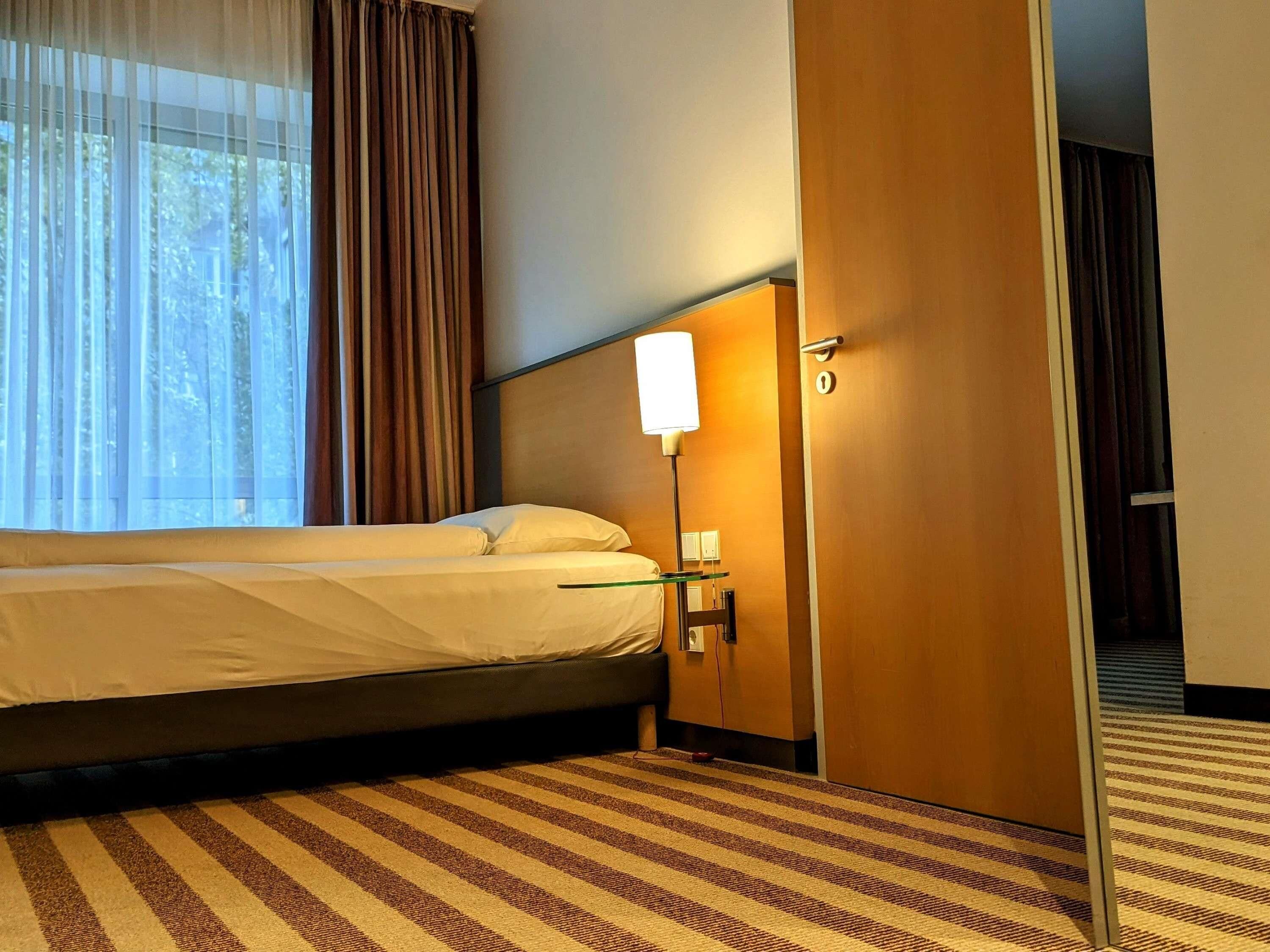Une chambre d’hôtel avec un lit, une table de chevet avec une lampe, une porte et un tapis à rayures.