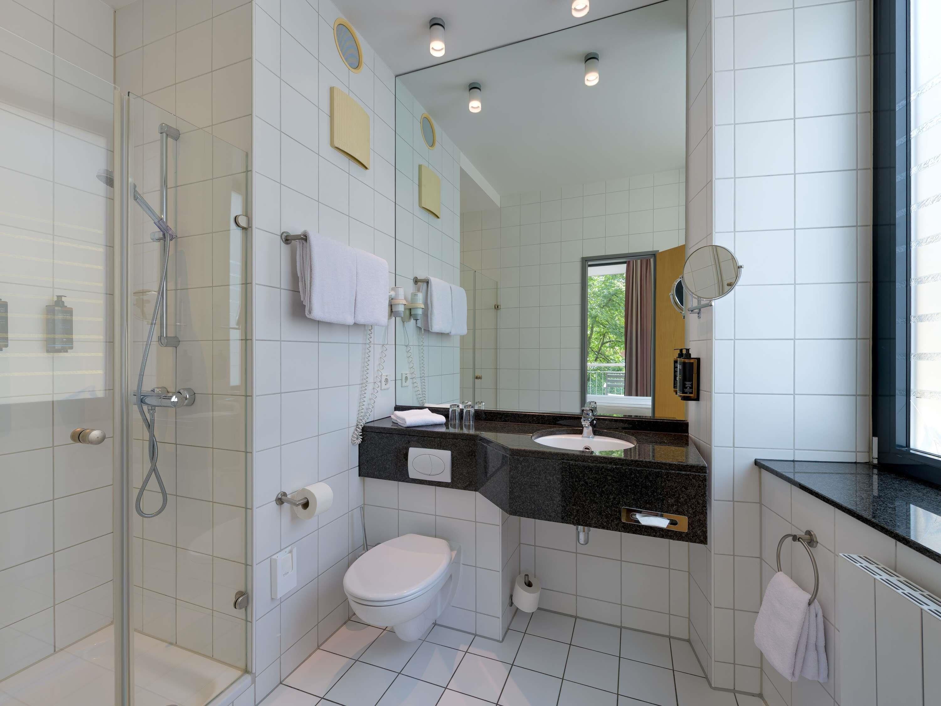 A modern bathroom with a glass-enclosed shower, a toilet, a sink with a black countertop, and a mirror.