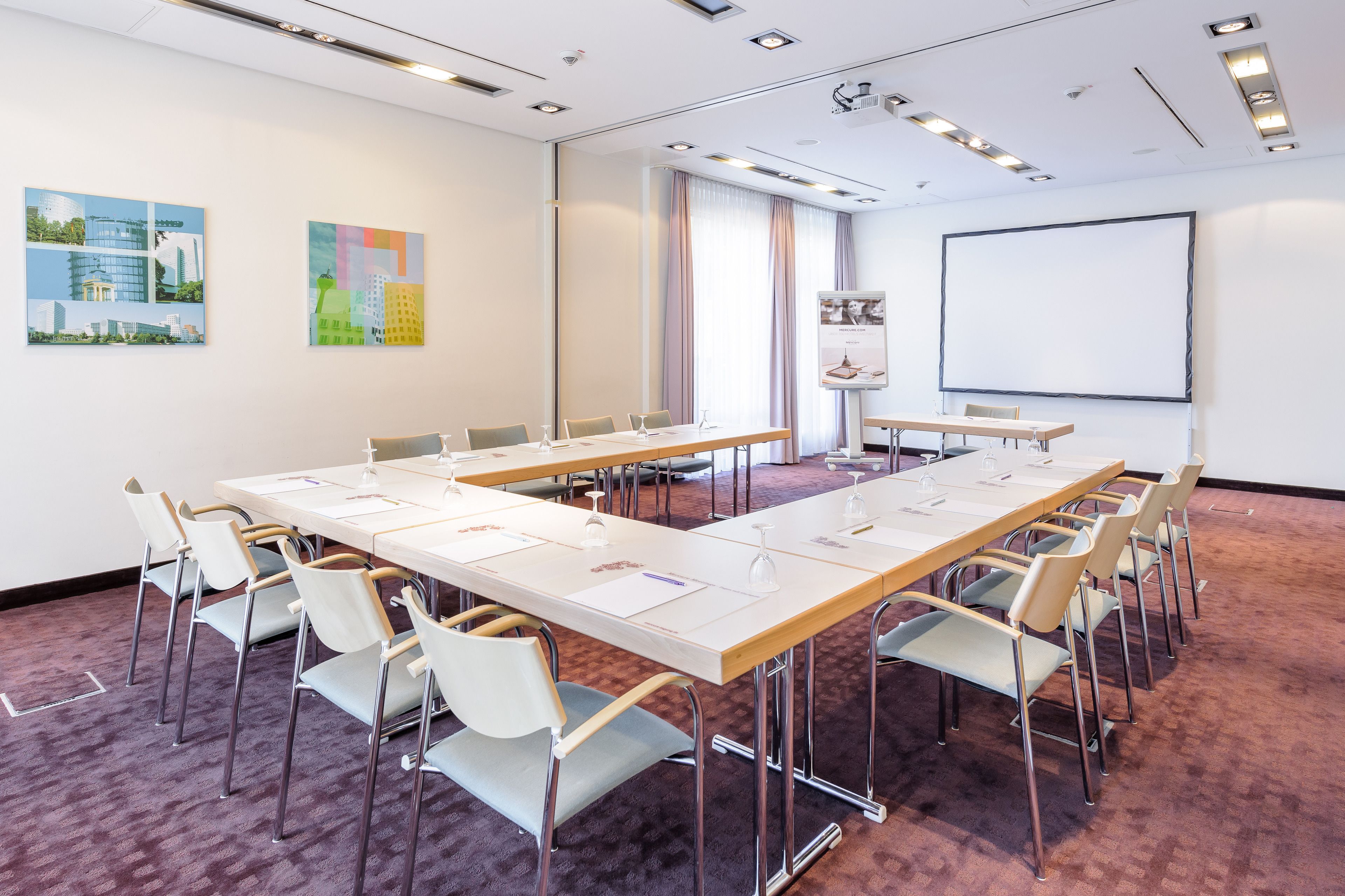 Ein Konferenzraum mit langem Tisch, Stühlen, einer Projektionsleinwand und Kunstwerken an den Wänden.
