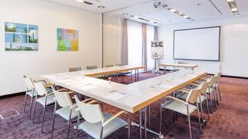 Ein Konferenzraum mit langem Tisch, Stühlen, einer Projektionsleinwand und Kunstwerken an den Wänden.