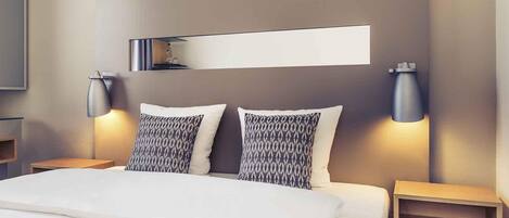 Una habitación de hotel con una cama, dos mesitas de noche, una estantería y dos lámparas de pared.