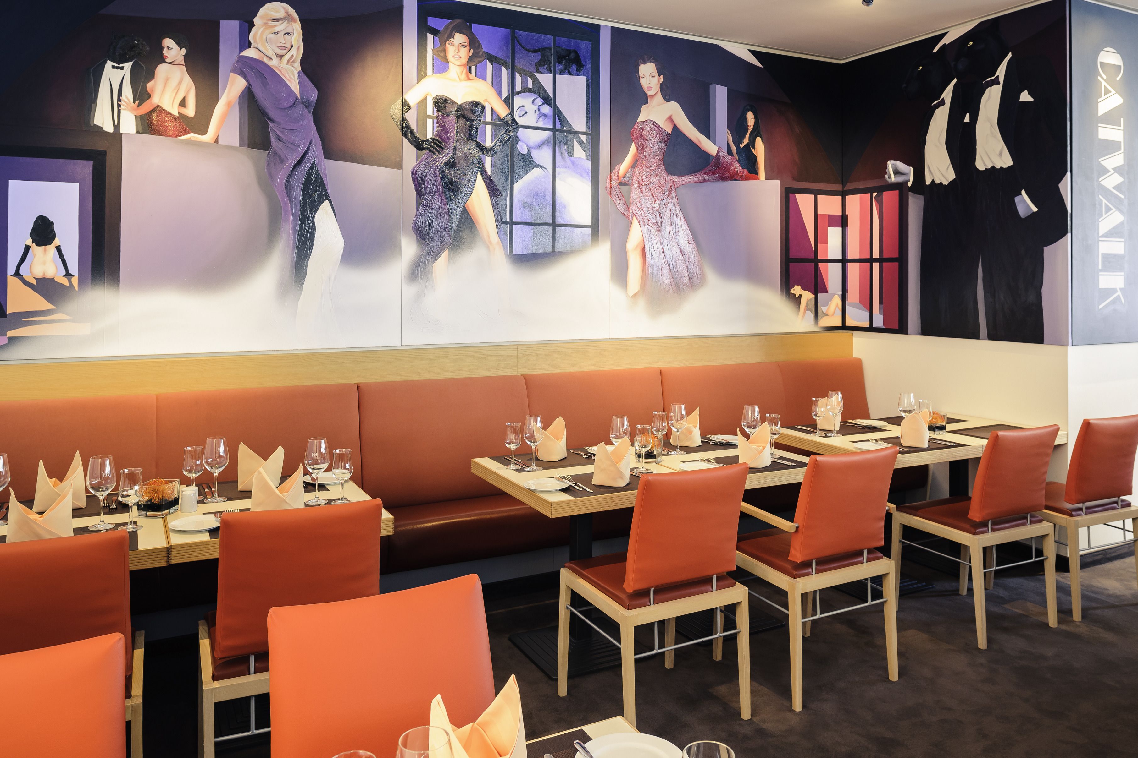 A restaurant with booths and tables, each set with wine glasses and plates.
