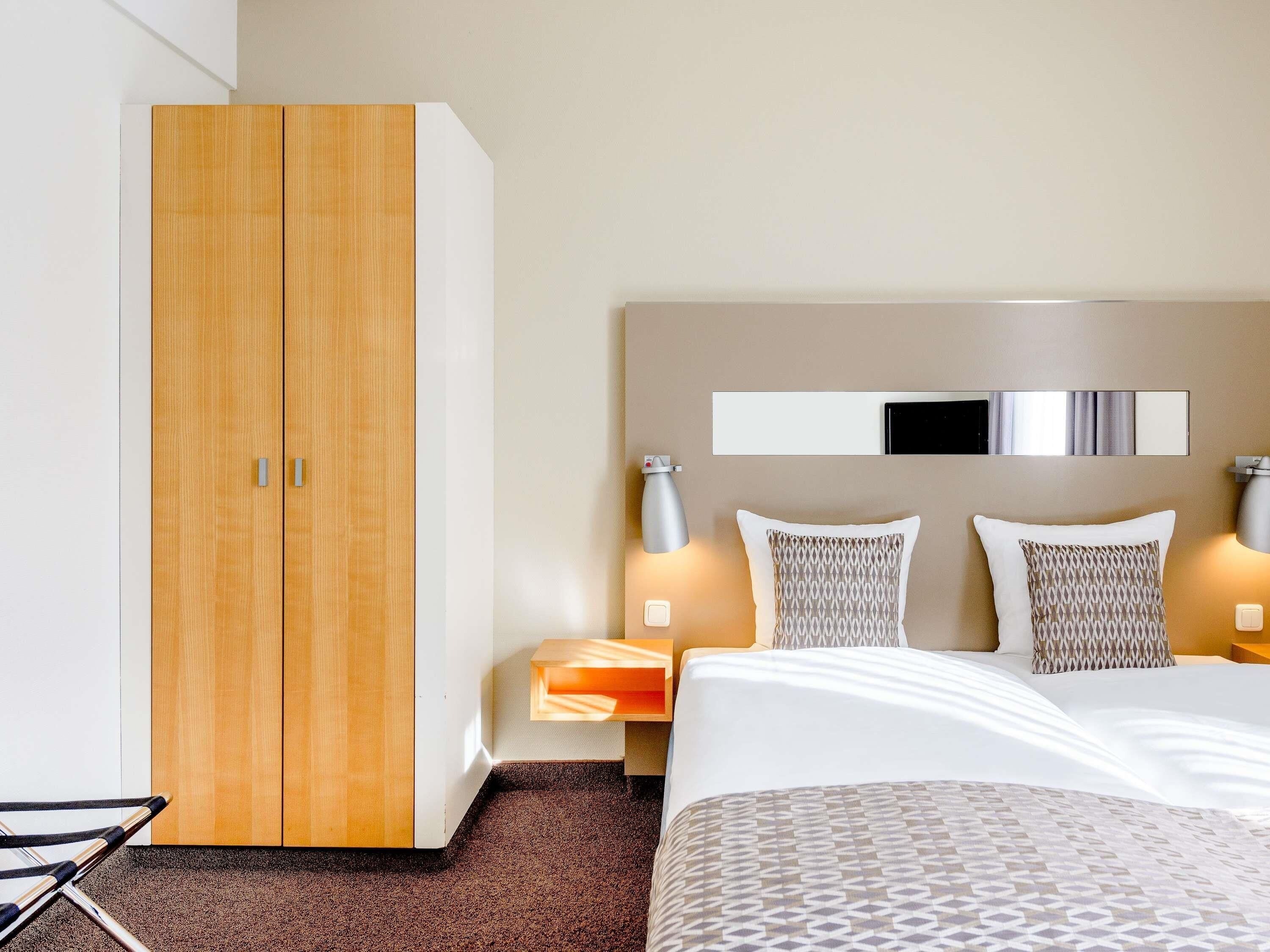 Quarto de hotel com cama, guarda-roupa, mesas de cabeceira e espelho.