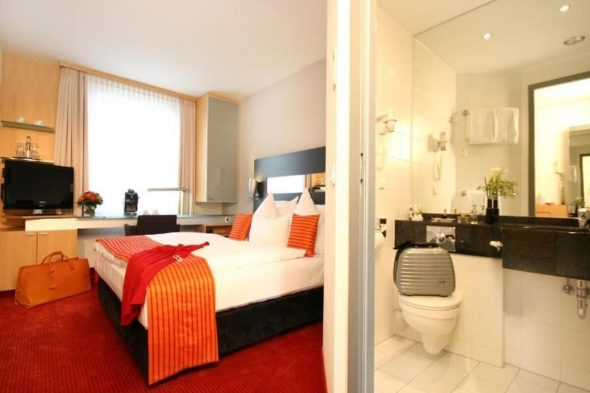 A hotel room with a bed, a desk, a TV, a bathroom, and a red carpet.