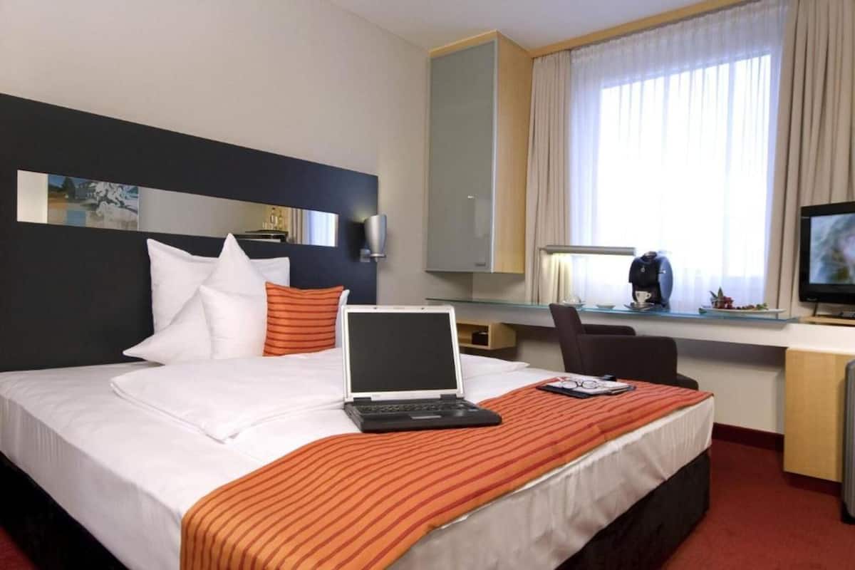A hotel room with a bed, a desk with a laptop, a television, and a window with curtains.