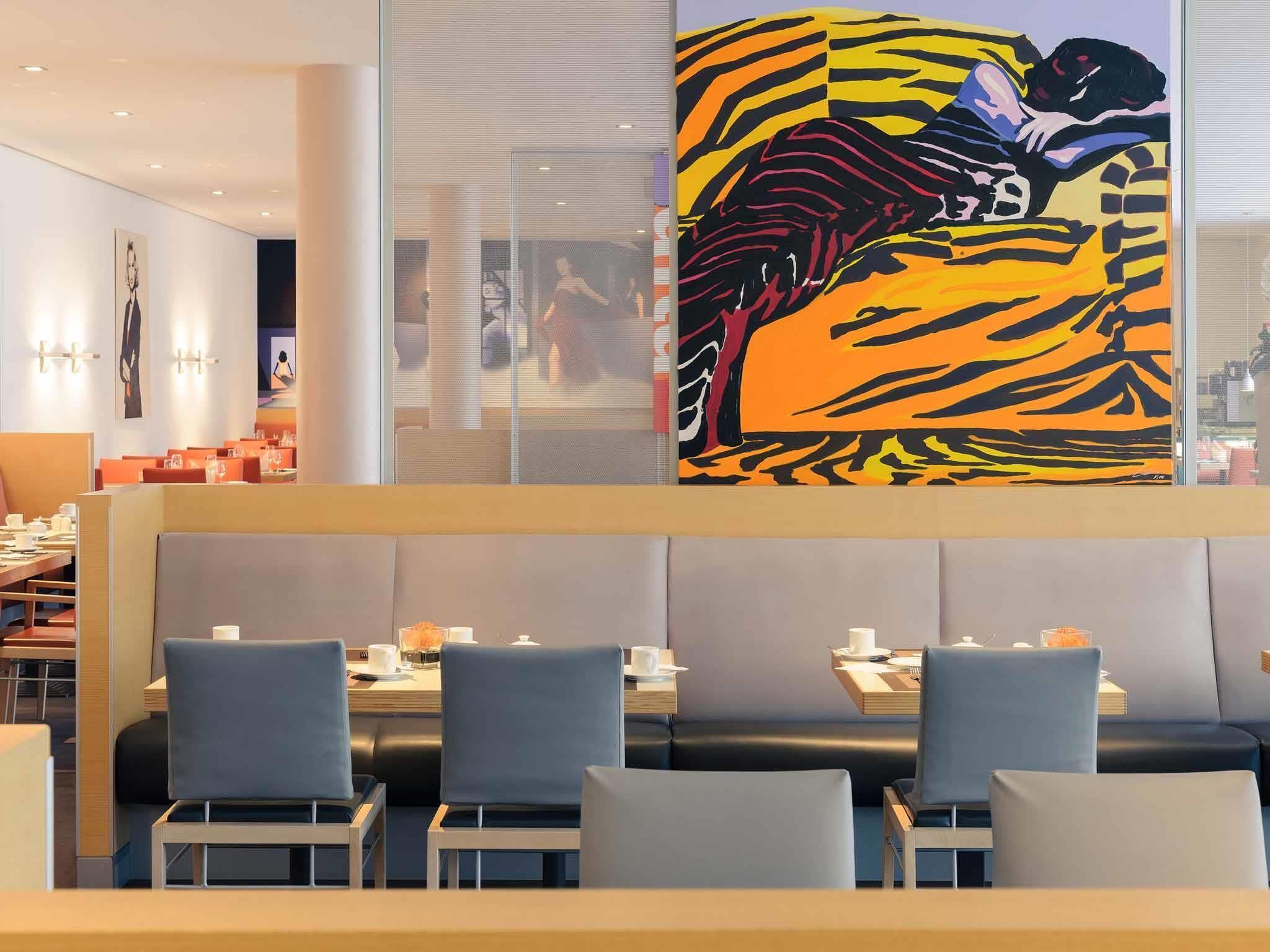 Ein modernes Restaurant mit Sitzboxen und Tischen, ein großes abstraktes Gemälde an der Wand und Blick auf die Stadt durch das Fenster.