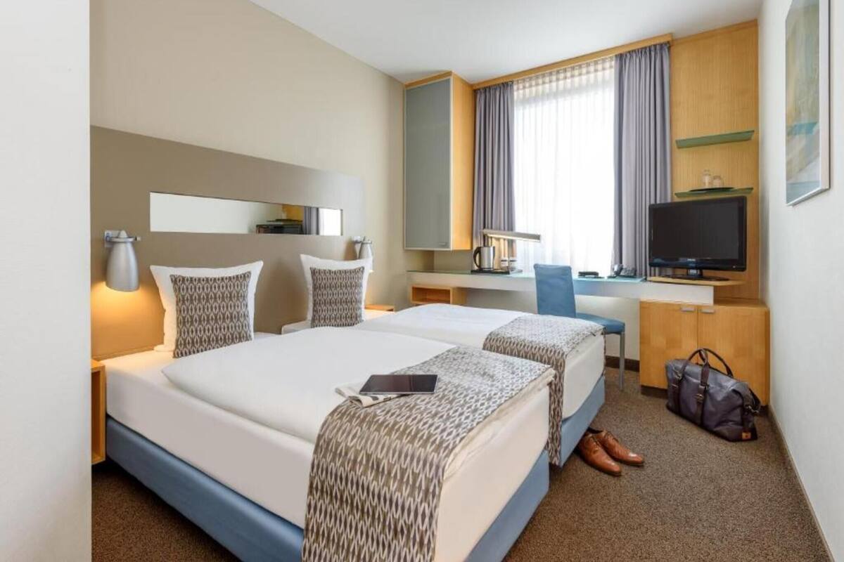 A hotel room with two beds, a desk, a television, and a mirror.