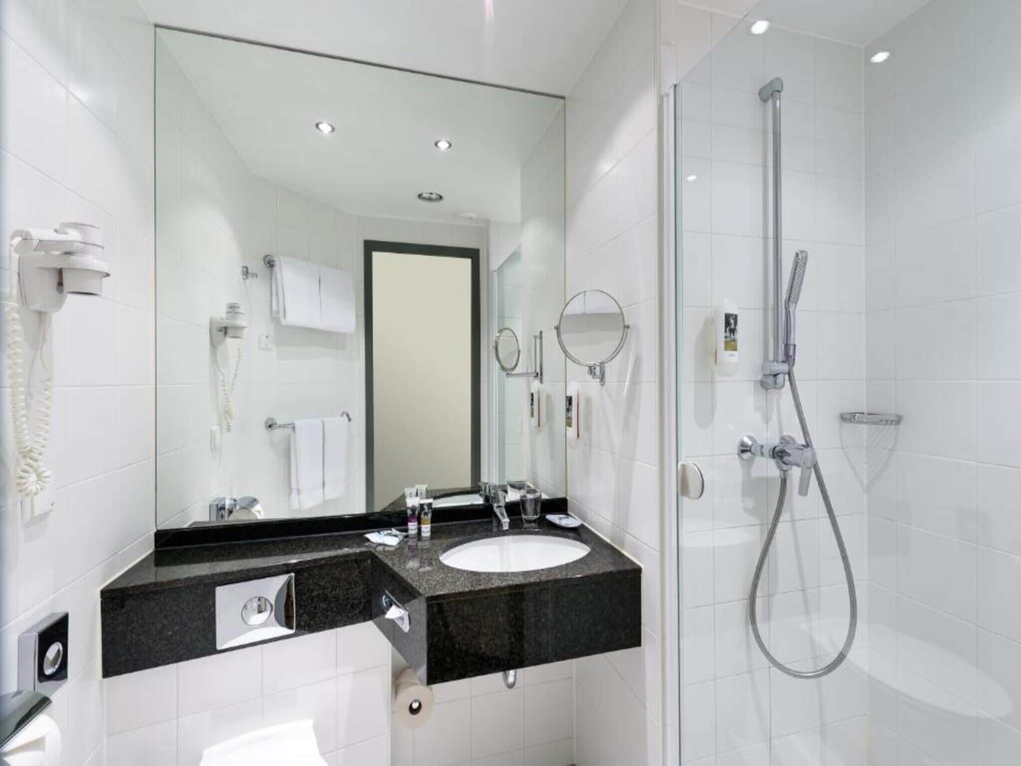 A modern bathroom with a glass-enclosed shower, a sink with a black countertop, and a large mirror.