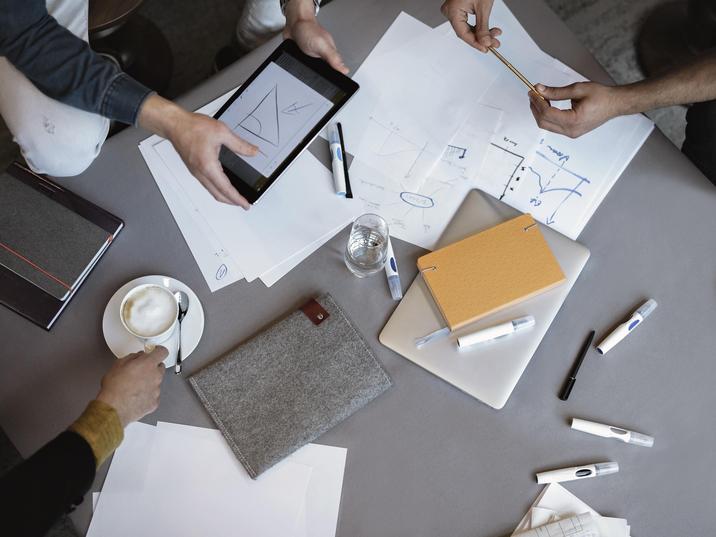 Una mesa con documentos, una tableta, un cuaderno, un bolígrafo, un vaso de agua y una taza de café.