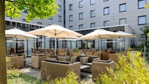A hotel courtyard with outdoor seating, including wicker furniture and umbrellas, and a modern building in the background.