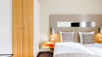 Ein Hotelzimmer mit Bett, Nachttischen, einem Kleiderschrank und einem Spiegel an der Wand.