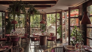 A restaurant with round tables and chairs, surrounded by large potted plants and natural light from large windows. - Seaside Palm Beach (San Bartolomé de Tirajana)