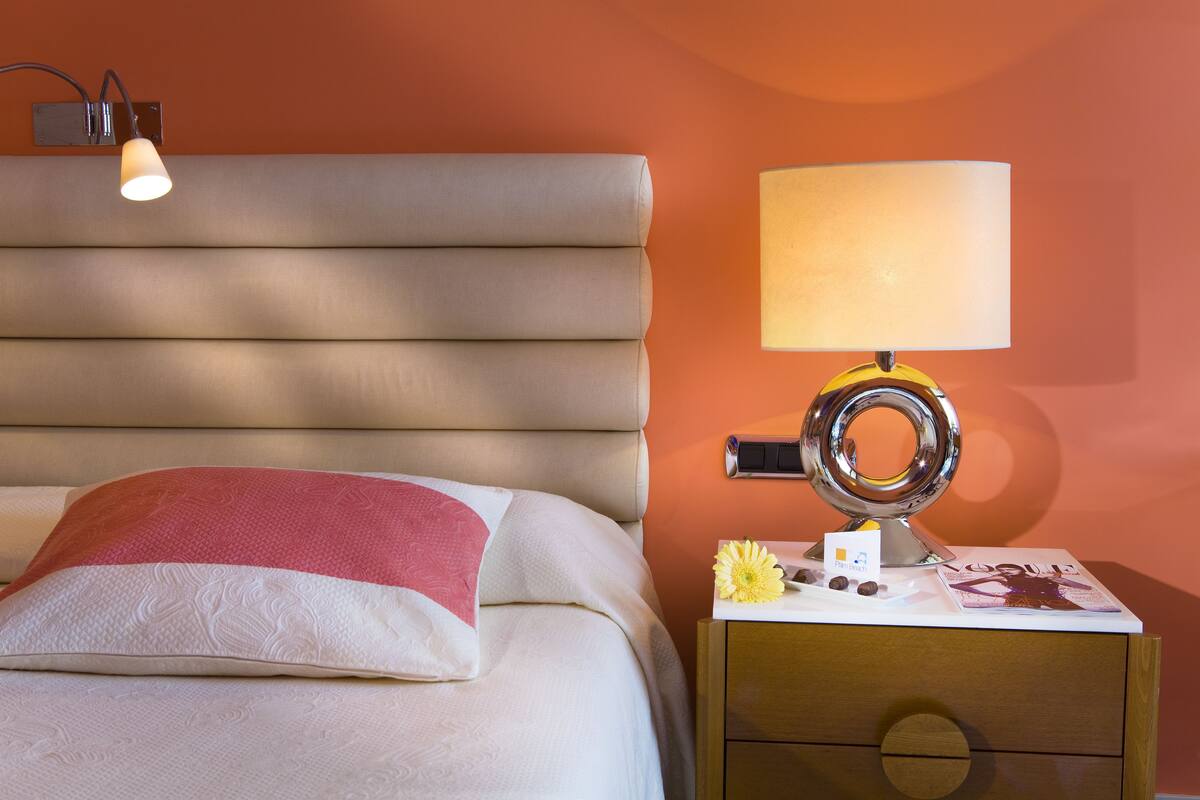 A neatly made bed with a pillow, a bedside lamp, and a magazine on a wooden nightstand.