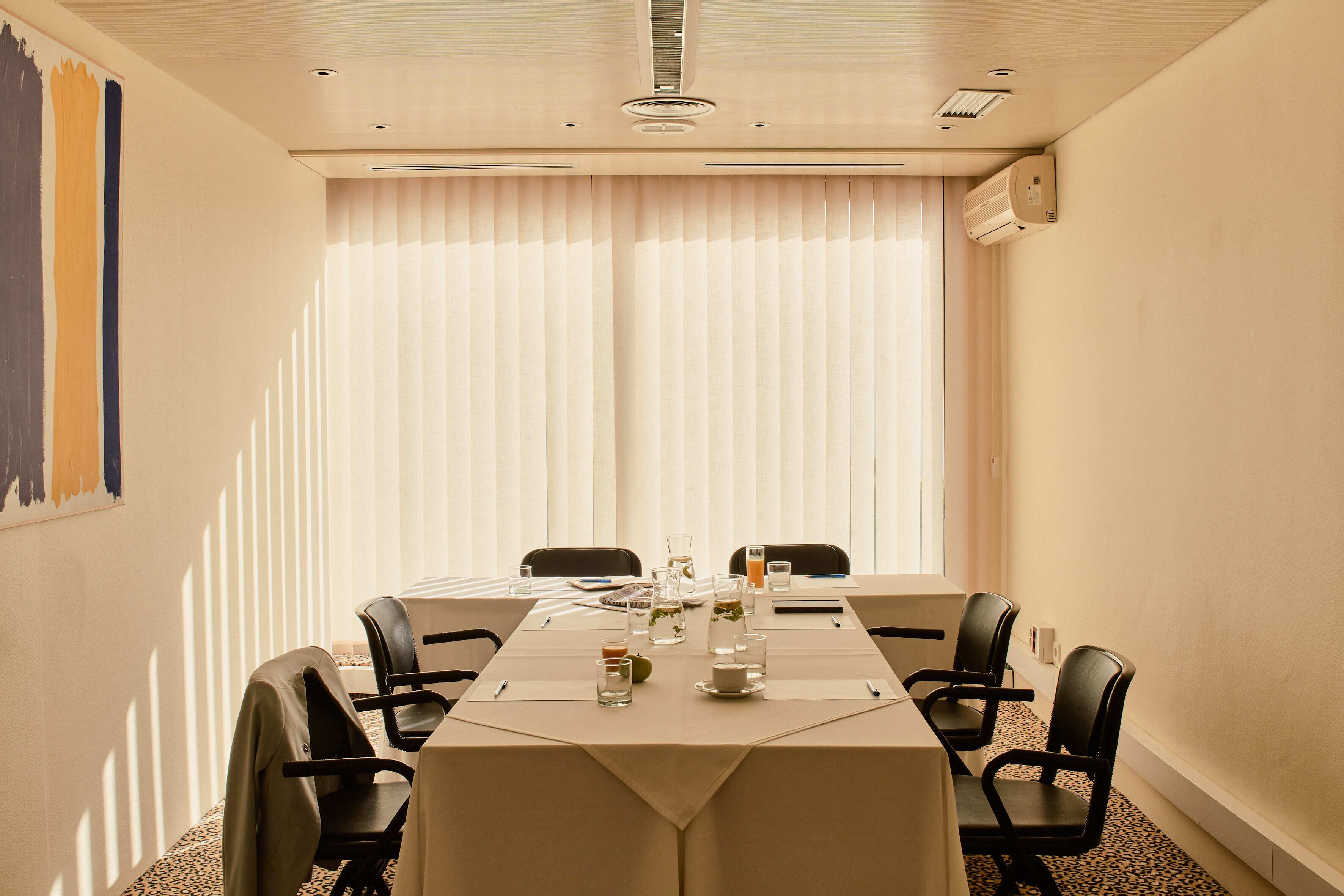 A conference room with a long table, chairs, and a large window with blinds.
