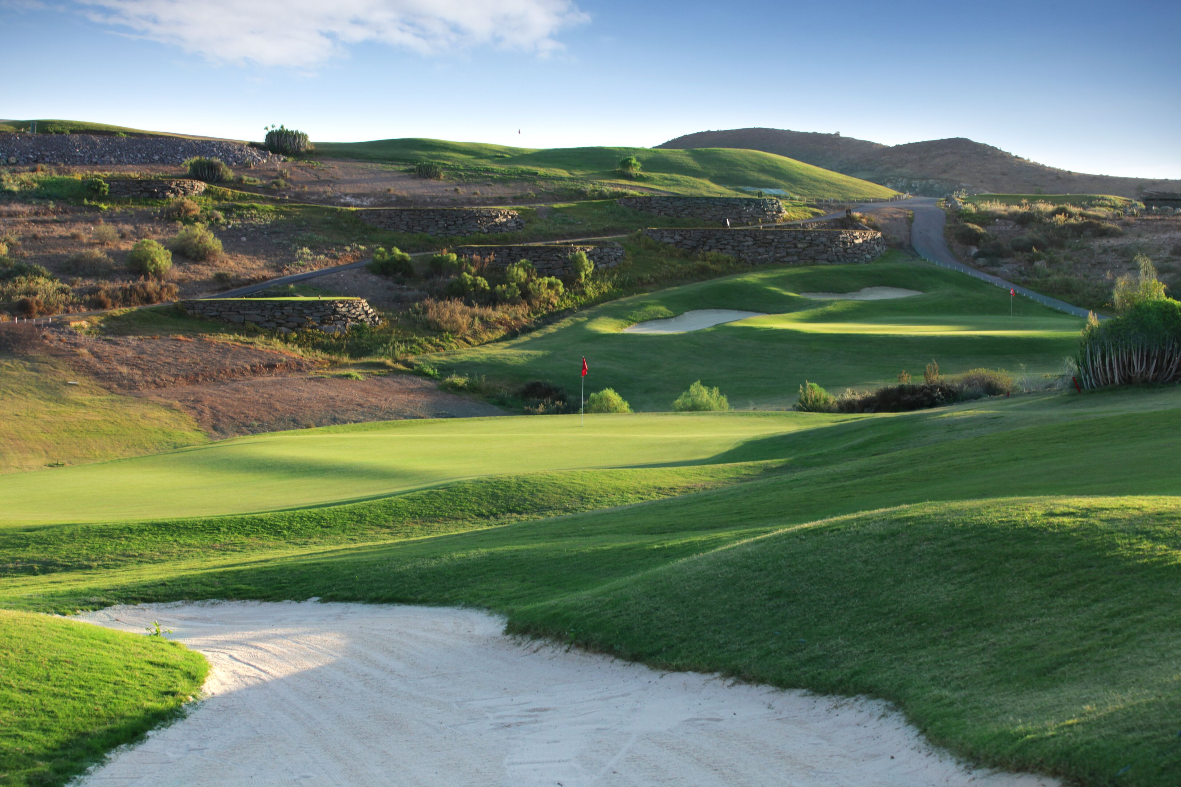 Un campo de golf con búnkeres de arena, una bandera y un muro de piedra.