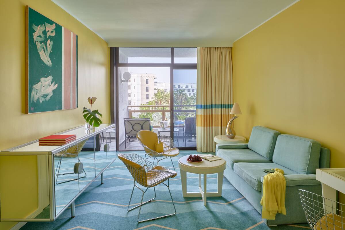 A modern hotel room with a balcony, a sofa, a dining table, and a chair.