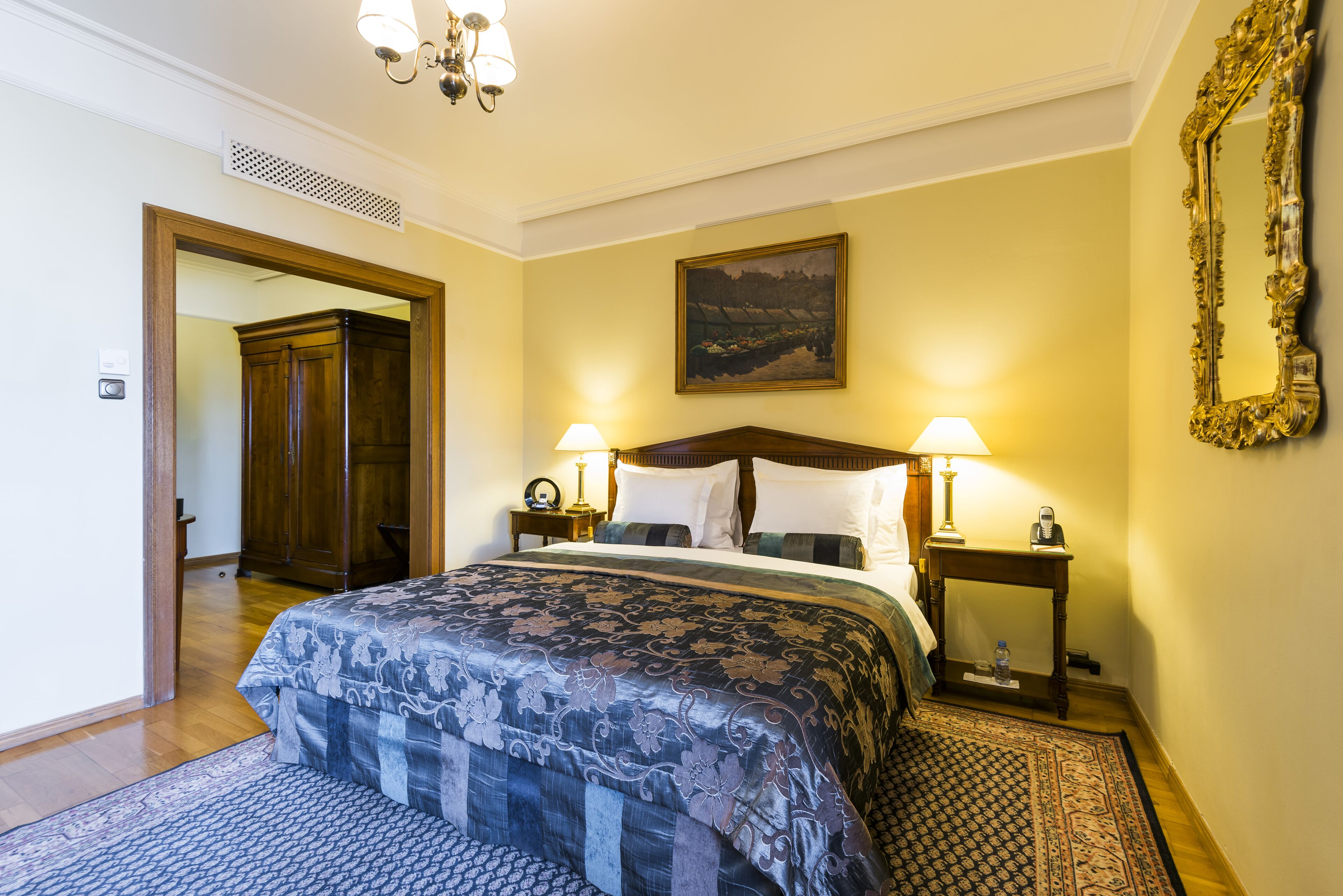 Habitación de hotel con una cama grande, dos mesitas de noche con lámparas, un armario de madera y un cuadro en la pared.