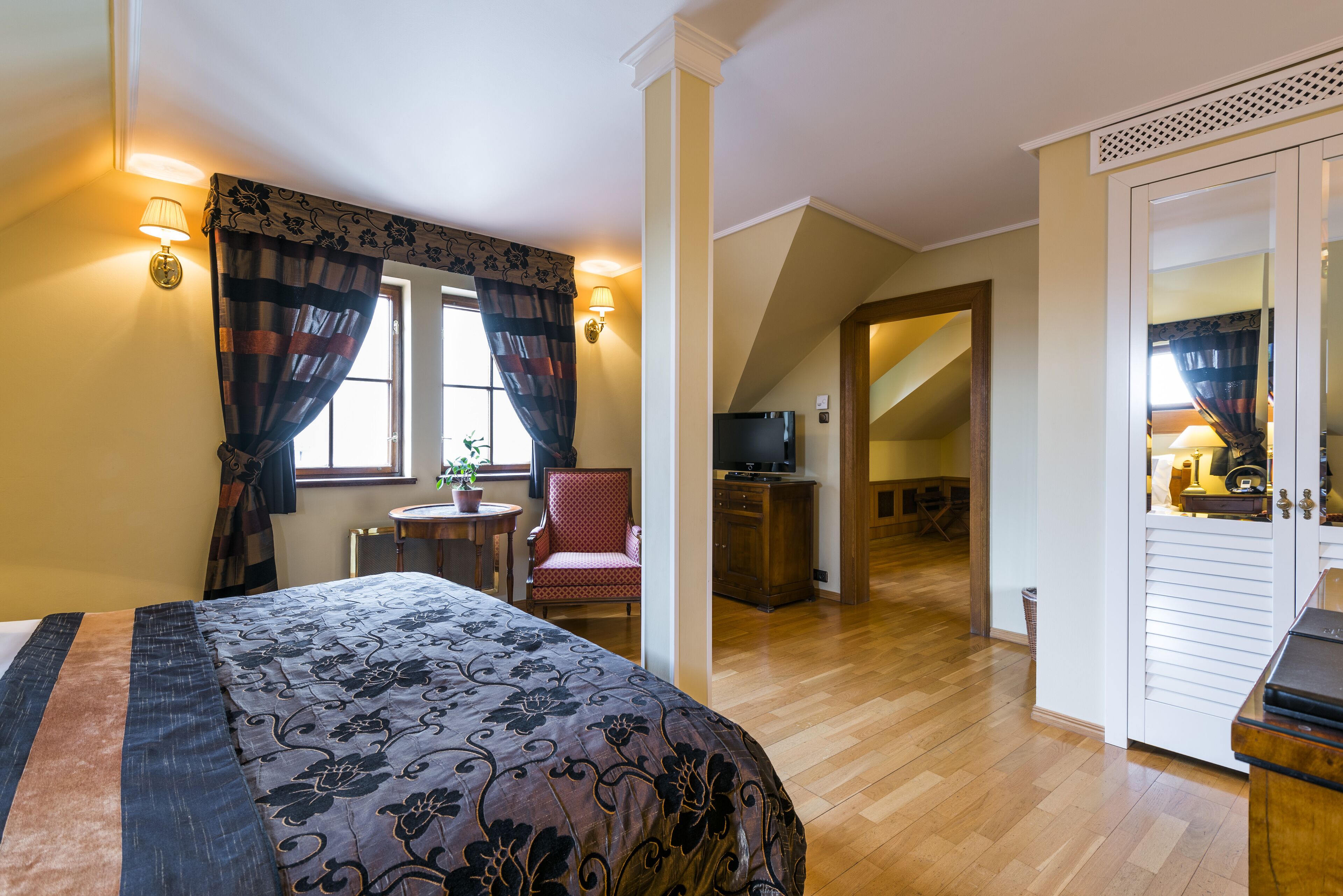A bedroom with a bed, a chair, a desk, a television, and a staircase leading to another room.