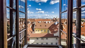 A view from a window overlooking a cityscape with red-tiled roofs and a clear blue sky. - Golden Well Hotel (Prague)