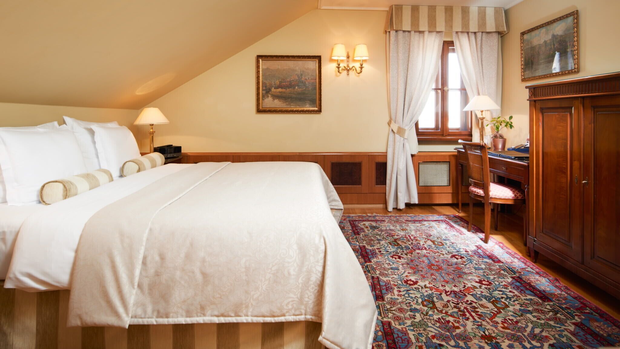 Une chambre d’hôtel avec un grand lit, un bureau avec une chaise, une armoire, un tapis à motifs et un tableau au mur.