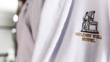 A white garment with an embroidered logo of a person standing next to a pedestal, and the text "GOLDEN WELL HOTEL" below it.