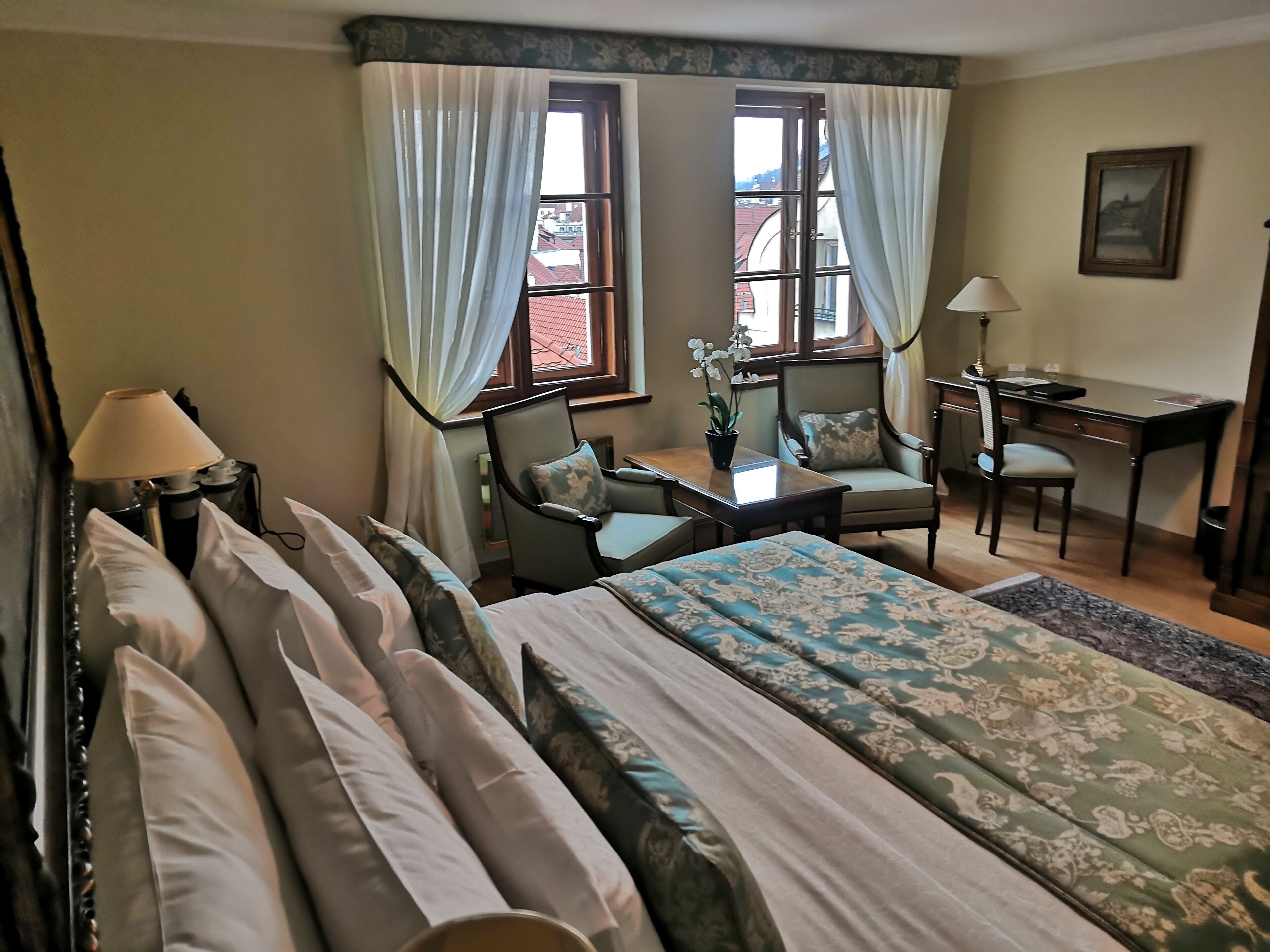 Una habitación de hotel con una cama, dos sillas, un escritorio y una ventana con cortinas.