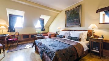 A hotel room with a large bed, a desk with a chair, a small table with a lamp, and a painting on the wall.
