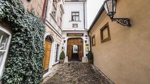 A cobblestone alleyway leading to a building with a wooden door and a sign reading "Ujstate stuane". - Golden Well Hotel (Prague)