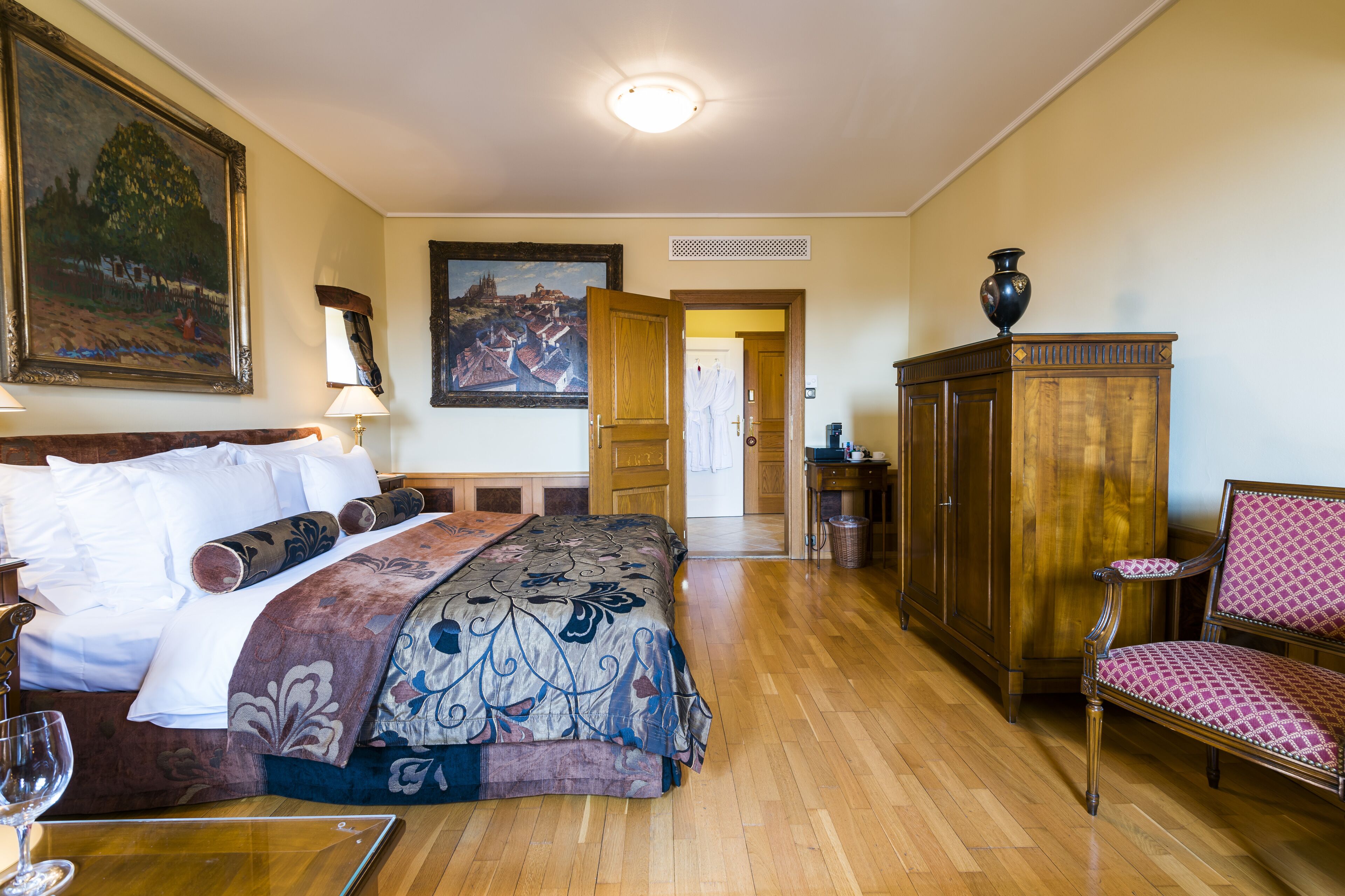 A hotel room with a bed, a chair, a cabinet, and a painting on the wall.