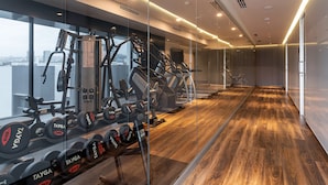 A modern gym with exercise equipment, large windows, and a wooden floor.