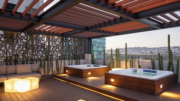 A rooftop terrace with wooden flooring, two hot tubs, a sofa, and a decorative wall.