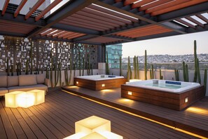 A rooftop terrace with wooden flooring, two hot tubs, a sofa, and a decorative wall.