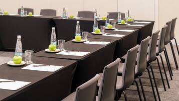 Une salle de conférence avec une longue table, des chaises, des bouteilles d’eau et des pommes posées sur la table.