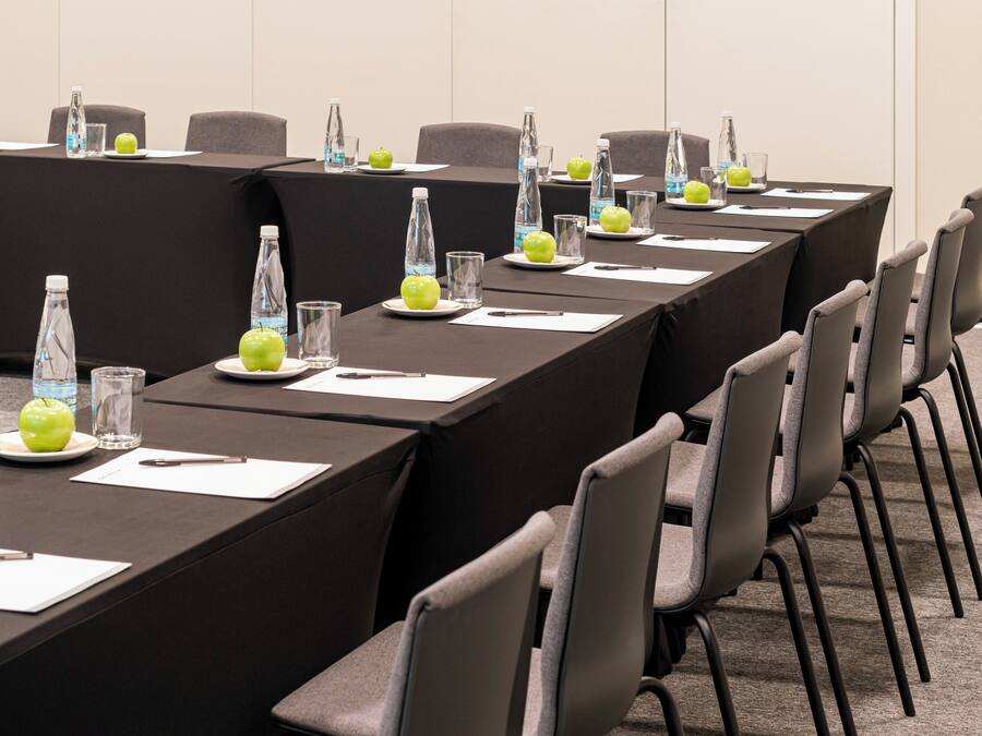 Une salle de conférence avec une longue table, des chaises, des bouteilles d’eau et des pommes posées sur la table.