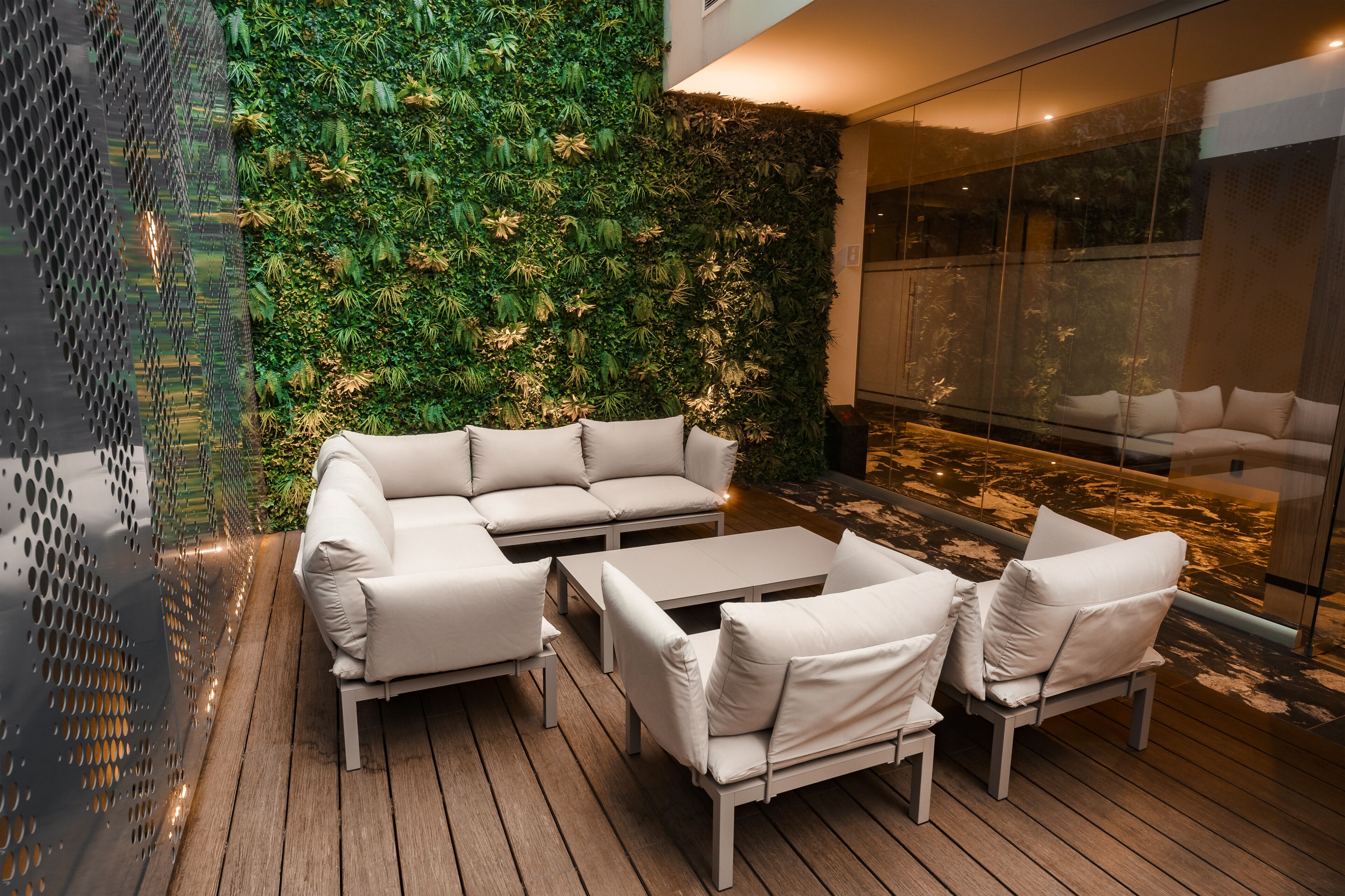 A modern outdoor seating area with a white sofa and tables, a wooden deck, and a green vertical garden wall.