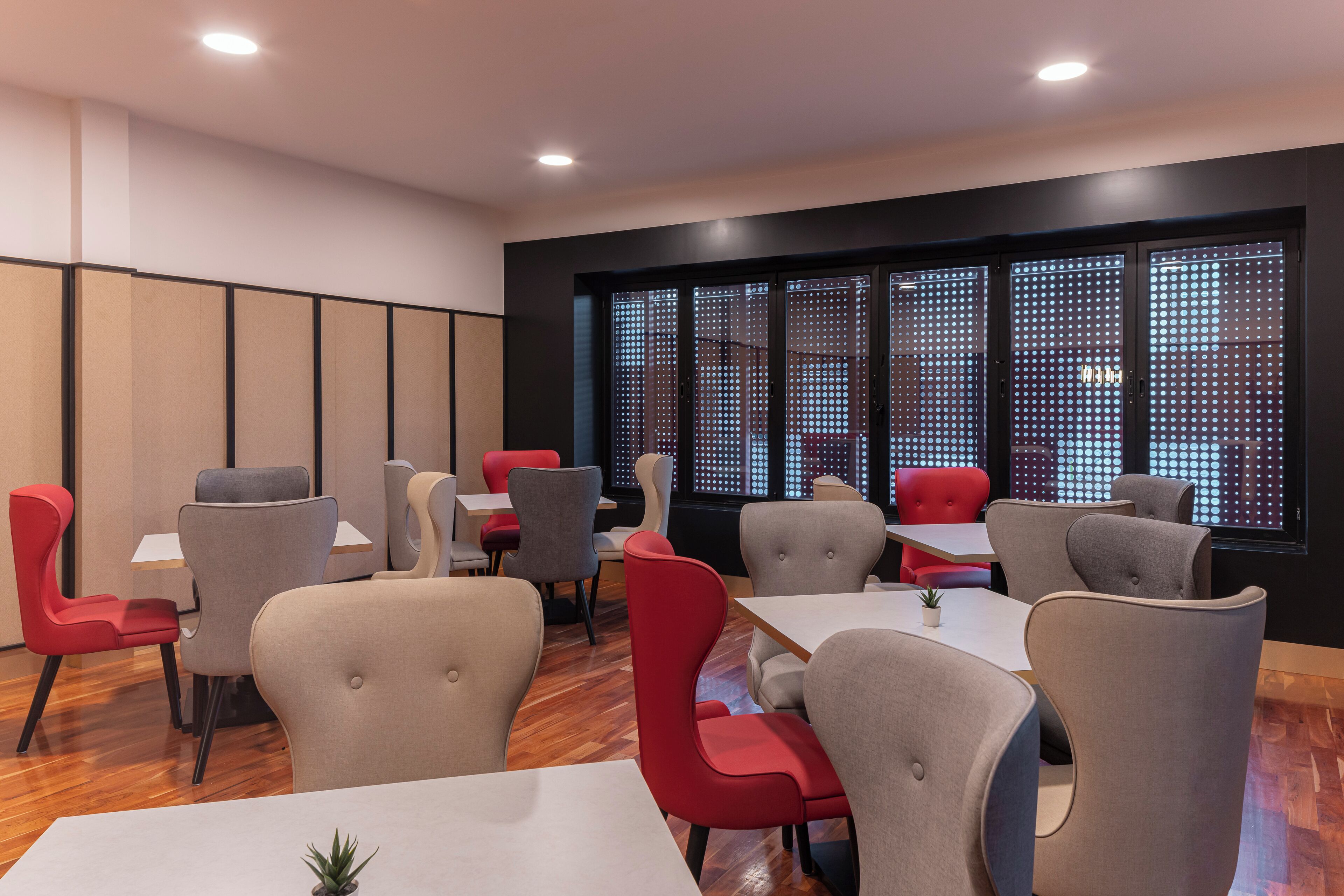 A modern dining area with tables and chairs, large windows with a patterned view, and a wooden floor.