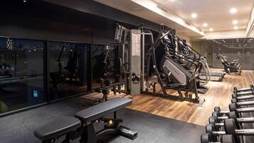A modern gym with various exercise equipment, a bench, and dumbbells.