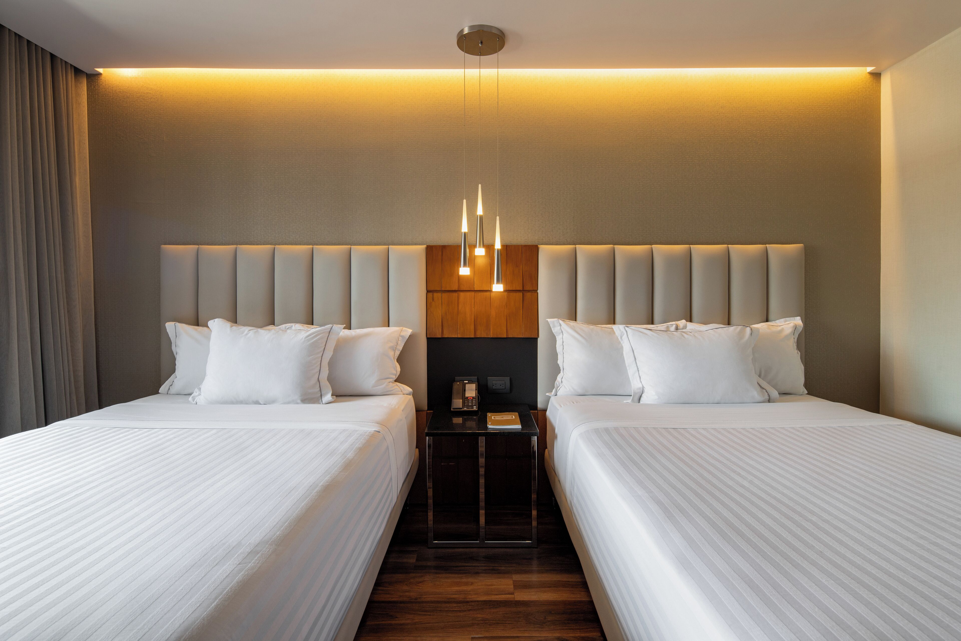 Habitación de hotel con dos camas, una mesita de noche y una lámpara colgante moderna.