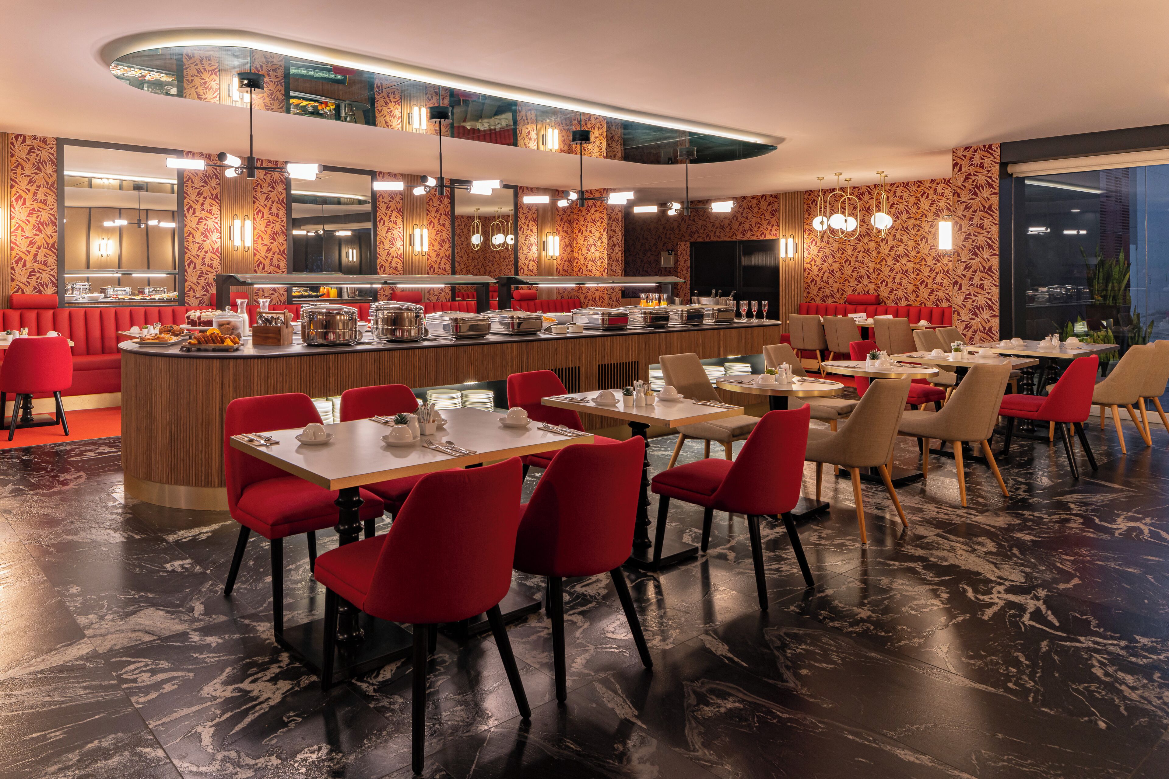 Un restaurant moderne doté d’un bar central, de sièges rouges et offrant une vue sur la ville la nuit.