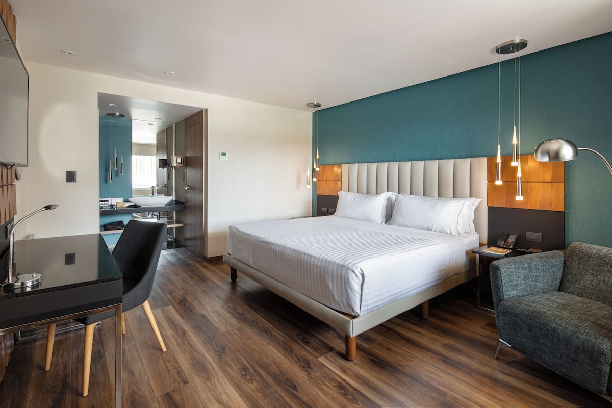 A modern hotel room with a large bed, a desk, a chair, and a sofa.