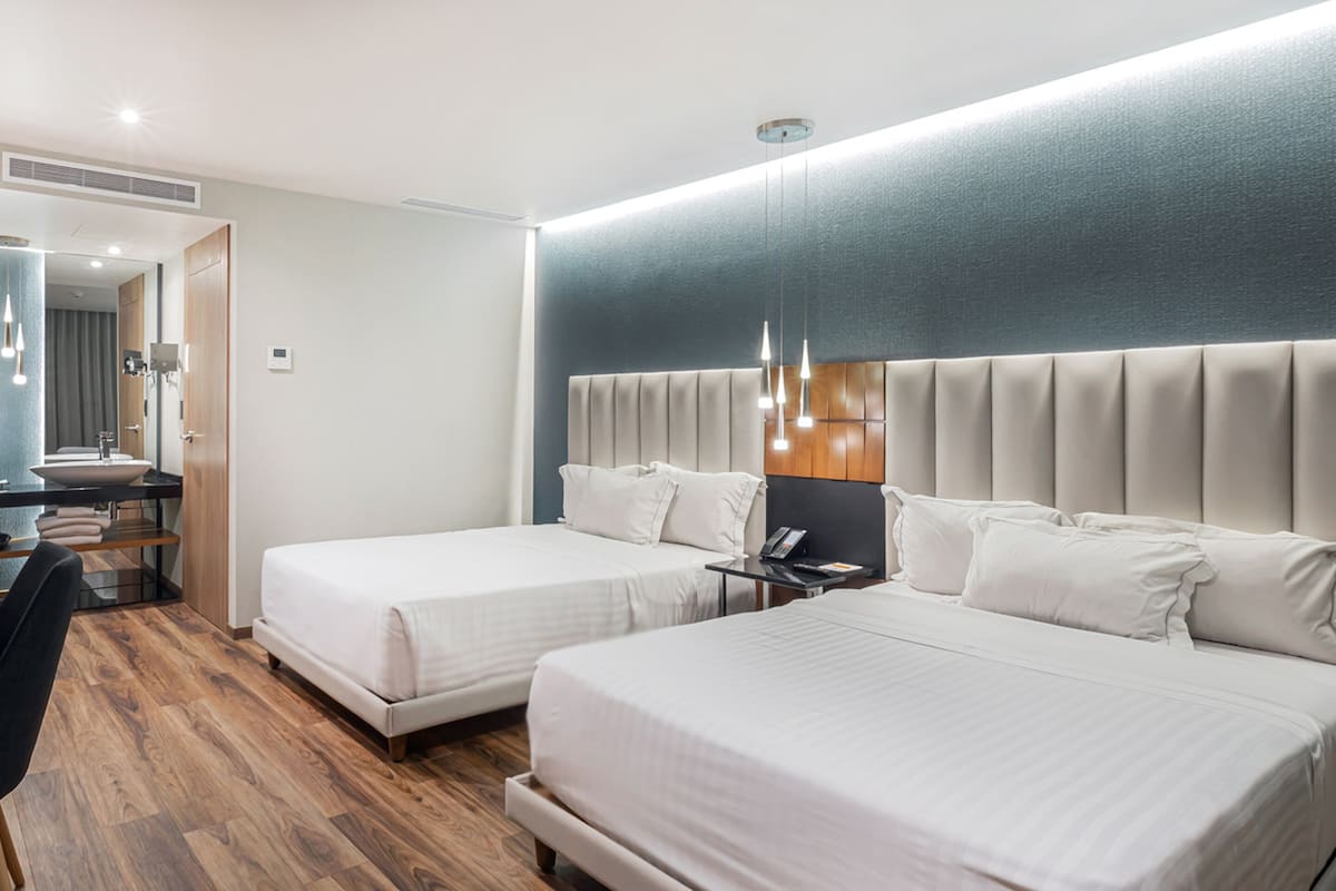 A hotel room with two beds, a desk, and a mirror.