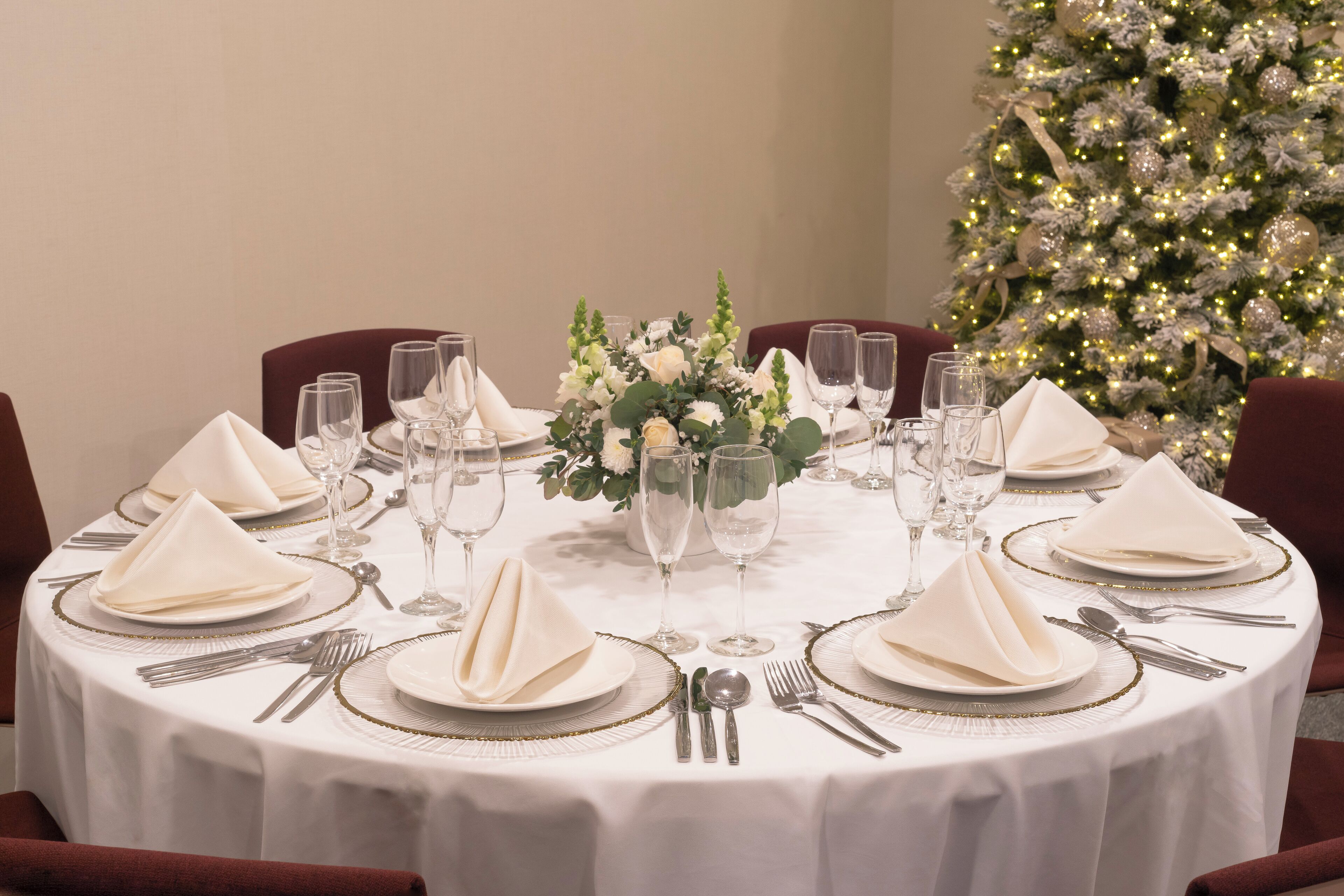 Una mesa redonda para cenar preparada para una comida formal, con manteles blancos, platos con borde dorado y cubiertos.