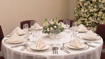 Una mesa redonda para cenar preparada para una comida formal, con manteles blancos, platos con borde dorado y cubiertos.
