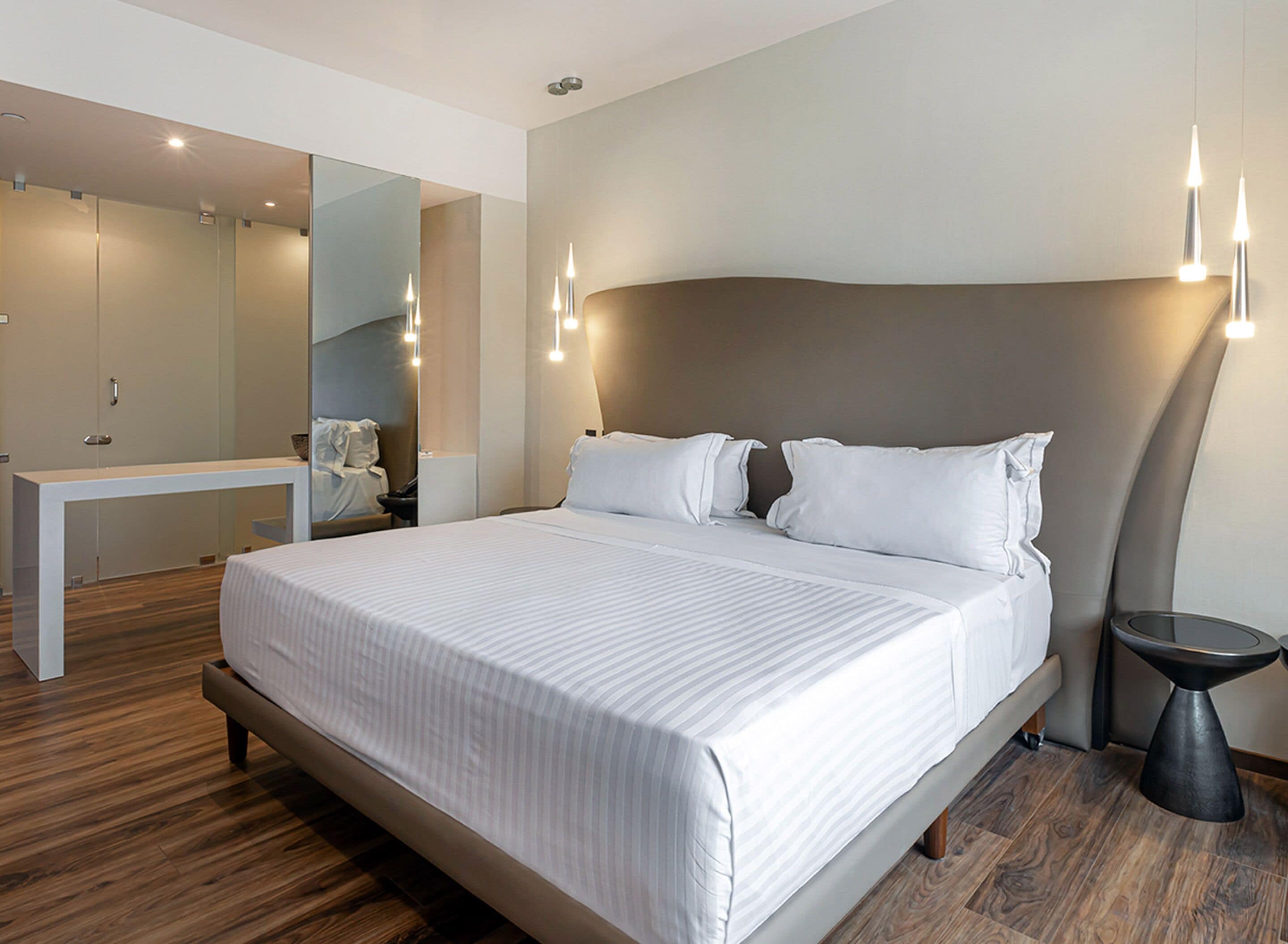 Een moderne hotelkamer met een groot bed, nachtkastjes, een spiegel en een klein rond tafeltje.