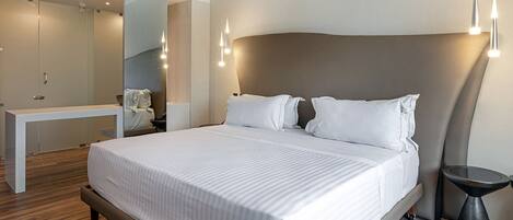 Una habitación de hotel moderna con una cama grande, mesitas de noche, un espejo y una pequeña mesa redonda.
