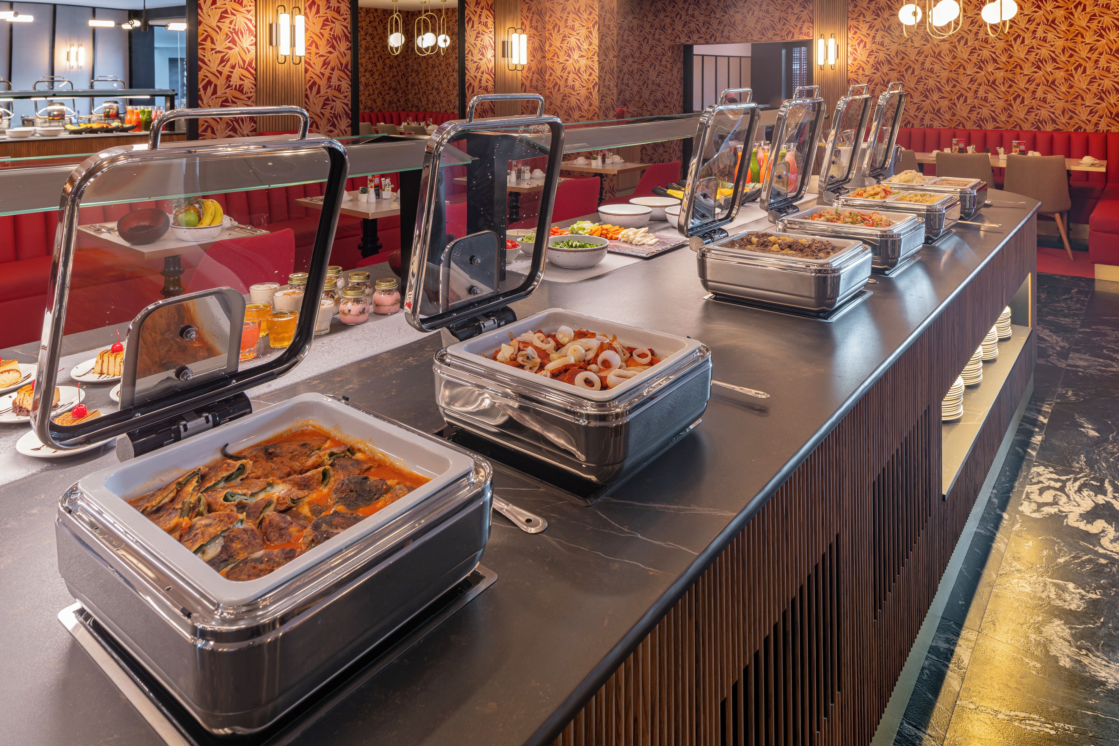 Un área de bufé con múltiples estaciones de servicio, cada una con tapas de vidrio transparente y diversas opciones de comida.