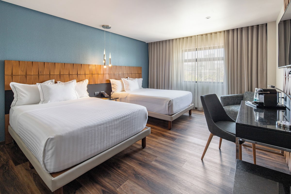 A hotel room with two beds, a desk, and a chair.