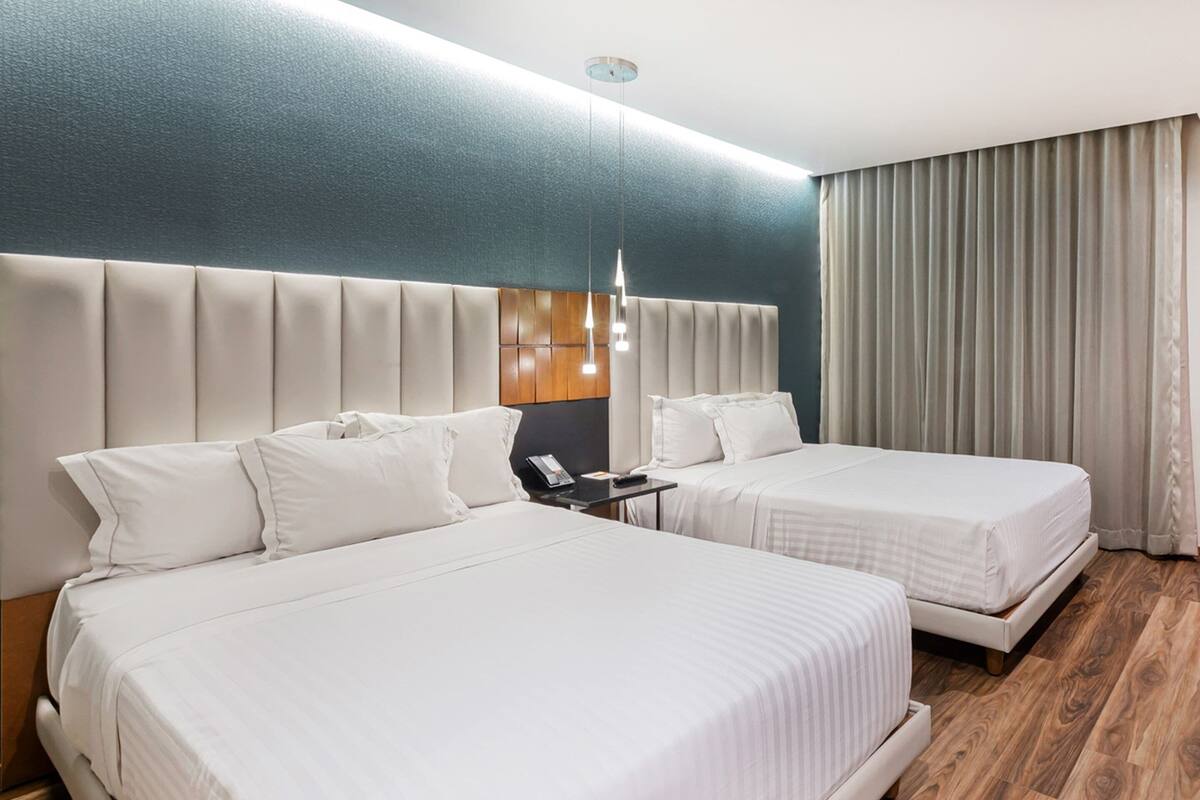A hotel room with two beds, a headboard, a nightstand, a phone, and a curtain.