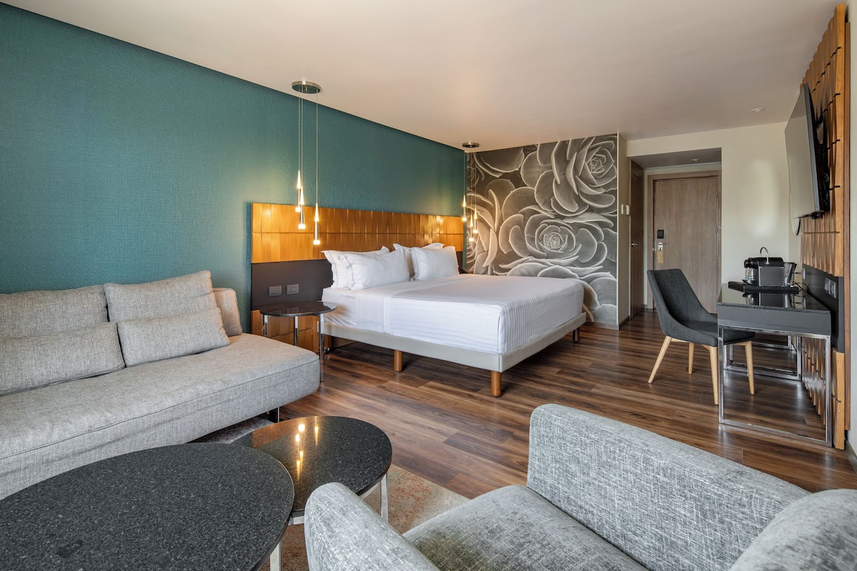 A modern hotel room with a bed, sofa, desk, and a decorative wall.