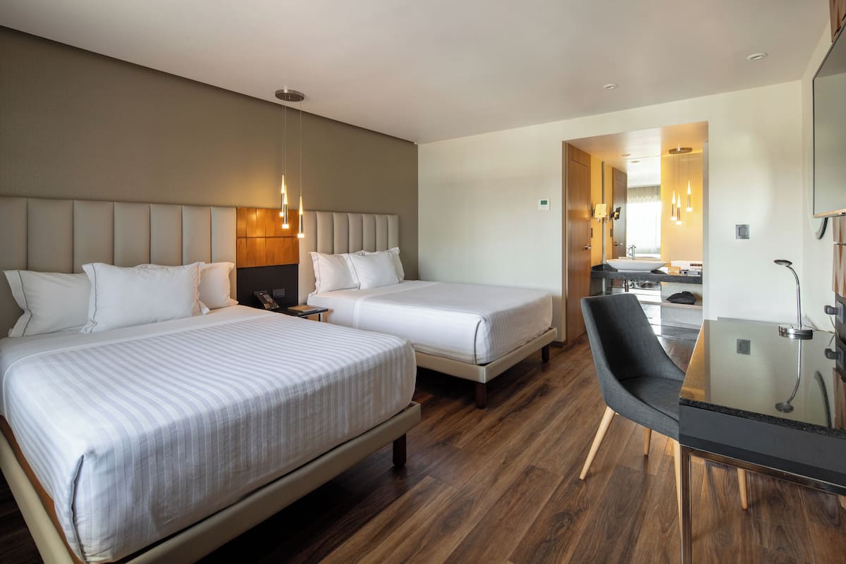 A hotel room with two beds, a desk, and a chair.